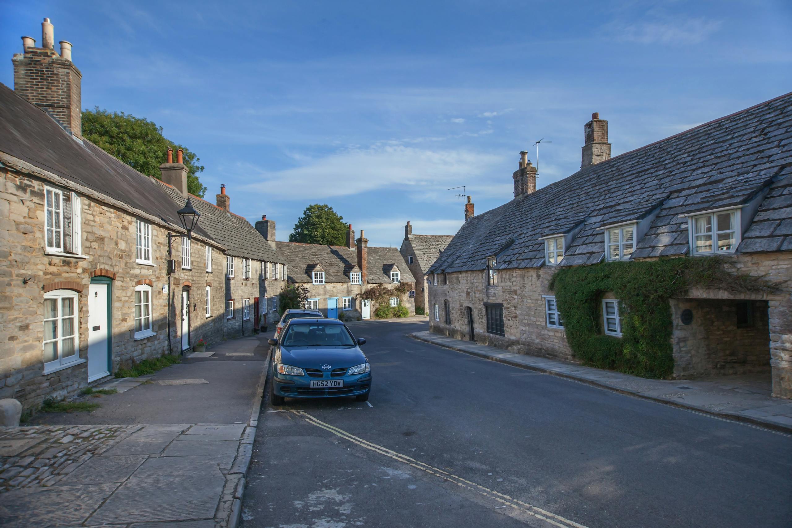 Quaint stone cottages line a picturesque street in Corfe, Dorset, England, under a clear blue sky.